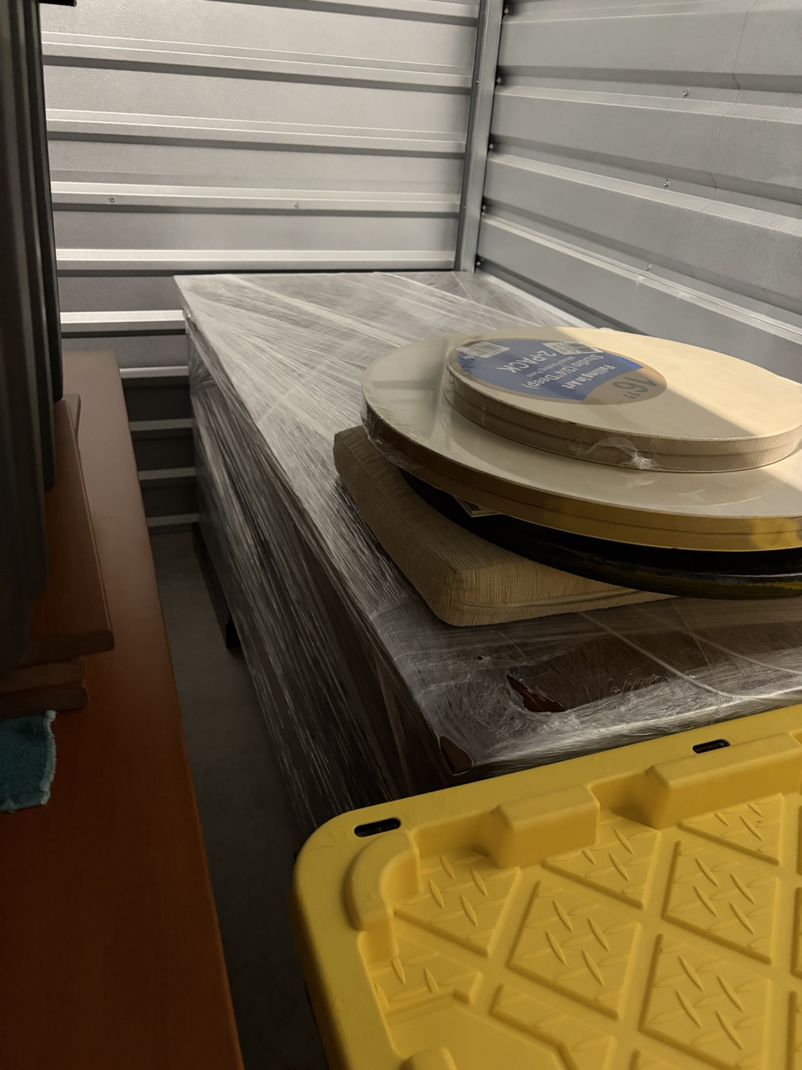 Shrink-wrapped table and stacked round tabletops with a seat cushion in a Nashville storage unit